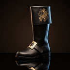 Pair, close together, buckles crossed: Pair of black leather Santa Claus boots with gold embroidered reindeer design on fold-over cuffs and engraved gold buckle straps
Pair, front-facing: Front view of black genuine leather Santa Claus boots showing gold thread reindeer embroidery and ornate gold buckle detail
Single boot, 3/4 profile: Single black leather Santa Claus boot with gold reindeer embroidery cuff and engraved buckle strap, side profile view